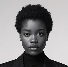 Black and white portrait of a woman with short curly hair wearing a dark turtleneck and blazer.